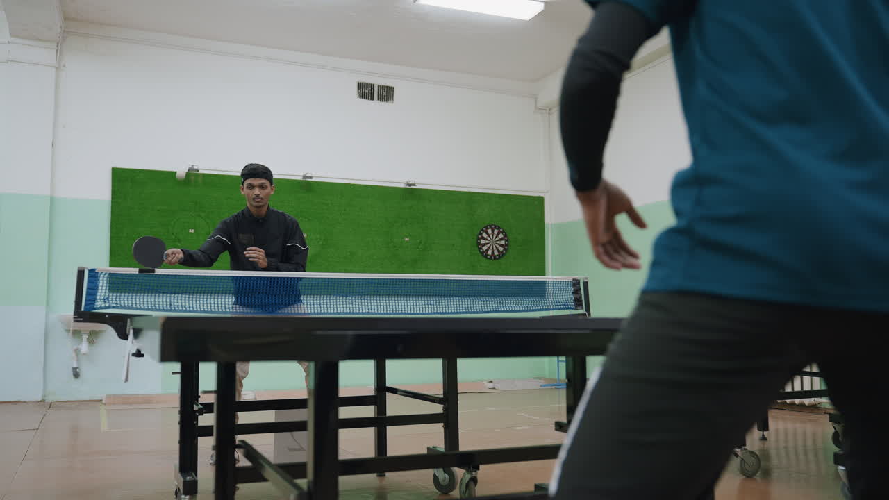 Training session of two table tennis players indoors as player in black jacket strikes ball into net during practice while opponent prepares across table symbolizing discipline