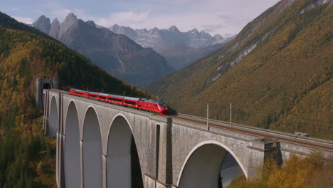 red train on a mountain viaduct in autumn