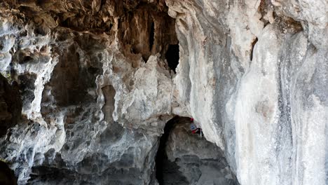 Rock-climber-abseiling-down-cave-rock-face,-extreme-sport-4K-aerial-view