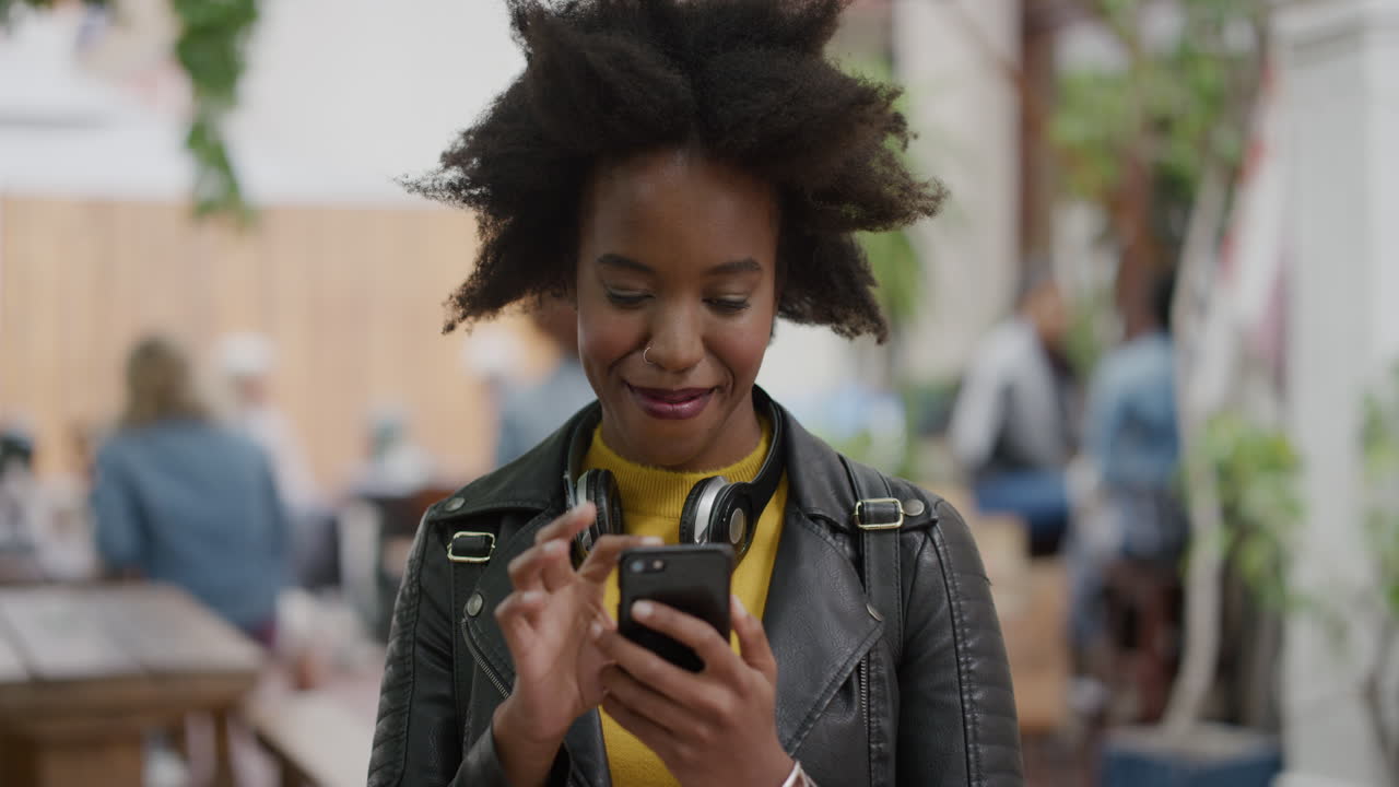 portrait of funky african american woman student smiling enjoying texting browsing online using smartphone stylish black woman in urban city