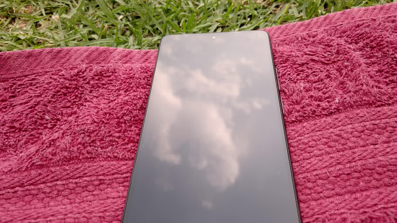 Pull out shot of green grass with a red towel and mobile phones on it during the day in a garden, outdoor, close up