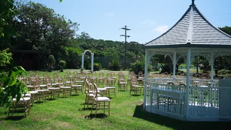 Atemberaubender-Hochzeitspavillon-Für-Eine-Hochzeit-Im-Freien-Unter-Den-Bäumen,-Begleitet-Von-Schönem-Sonnigem-Wetter-Und-Einer-Schönen-Aufstellung-Von-Goldenen-Stühlen-Für-Die-Gäste