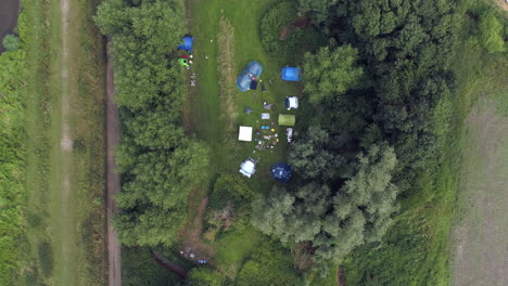 wide shot aerial drone footage from above with tents zooming out from a campsite revealing a forest and trees in the countryside