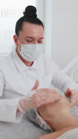 beautician applying special moisturizing cream scrub peeling face of pretty caucasian woman girl