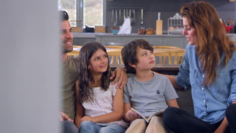 familia sentada en el sofá en la sala de estar hablando y leyendo un libro juntos