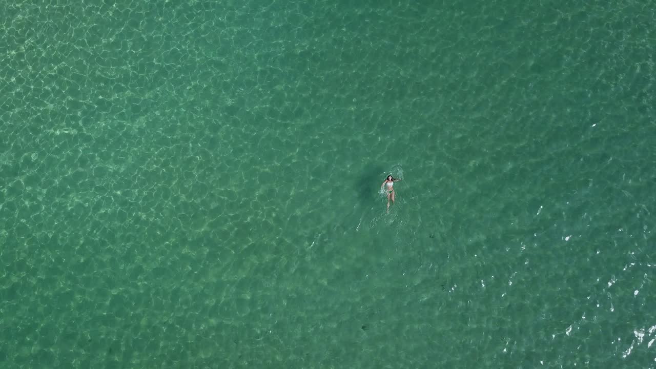Female tourist swims on her back in the clear, shimmering, green waters of the Aegean Sea