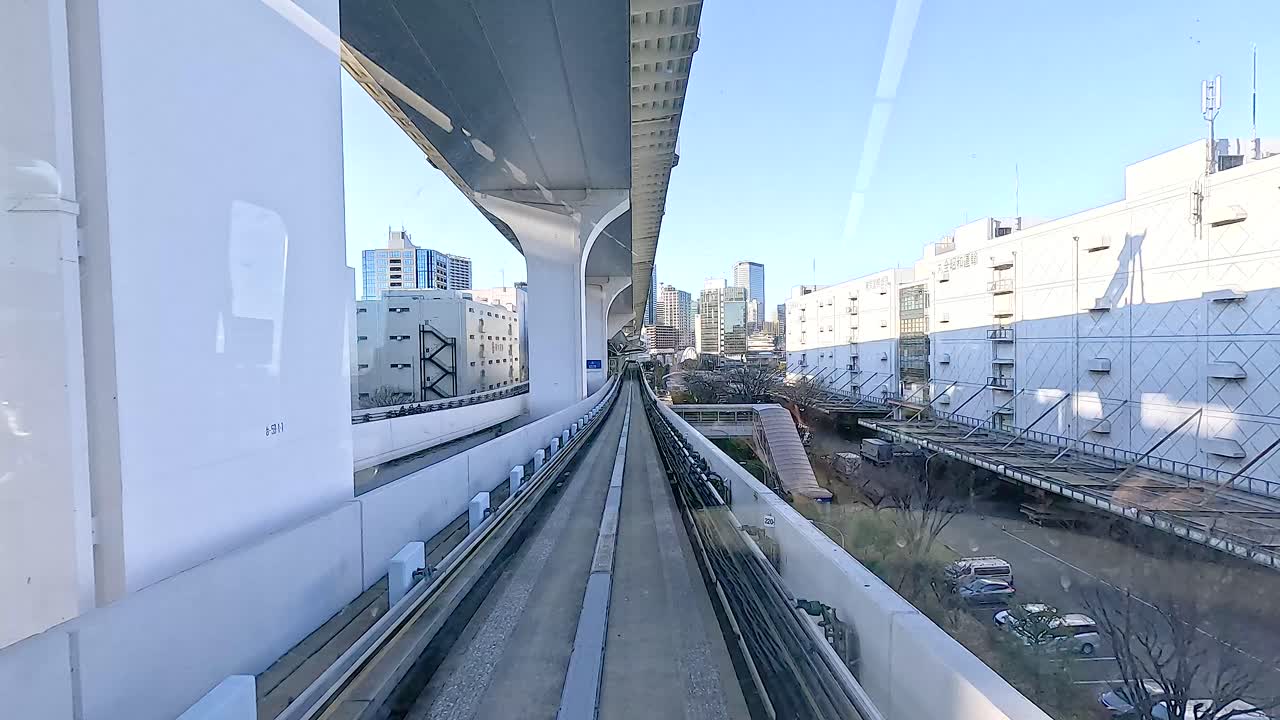 A monorail glides through Tokyo's urban environment, showcasing modern architecture and clear skies in a dynamic cityscape