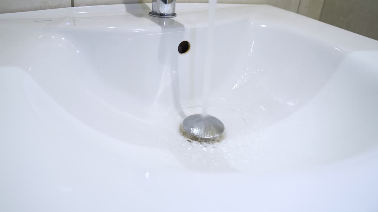 Clean close-up of water running into drain in modern white sink. Useful for hygiene, plumbing, or minimalist design projects.
