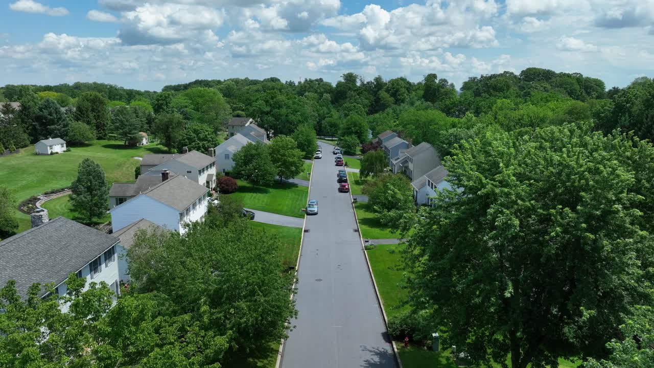 Aerial backwards shot of American housing area with wide road and driving vehicle in summer