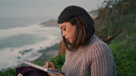 una mujer artista dibujando un paisaje marino sentada en la costa de cerca. una chica disfruta de su pasatiempo.