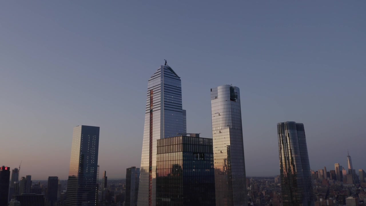 Le torri di vetro di Hudson Yards si ergono su Manhattan sotto un cielo serale soffuso al crepuscolo, con un magnifico bagliore delicato e il riflesso della luce gialla che scintilla sul vetro, sfondo aereo.