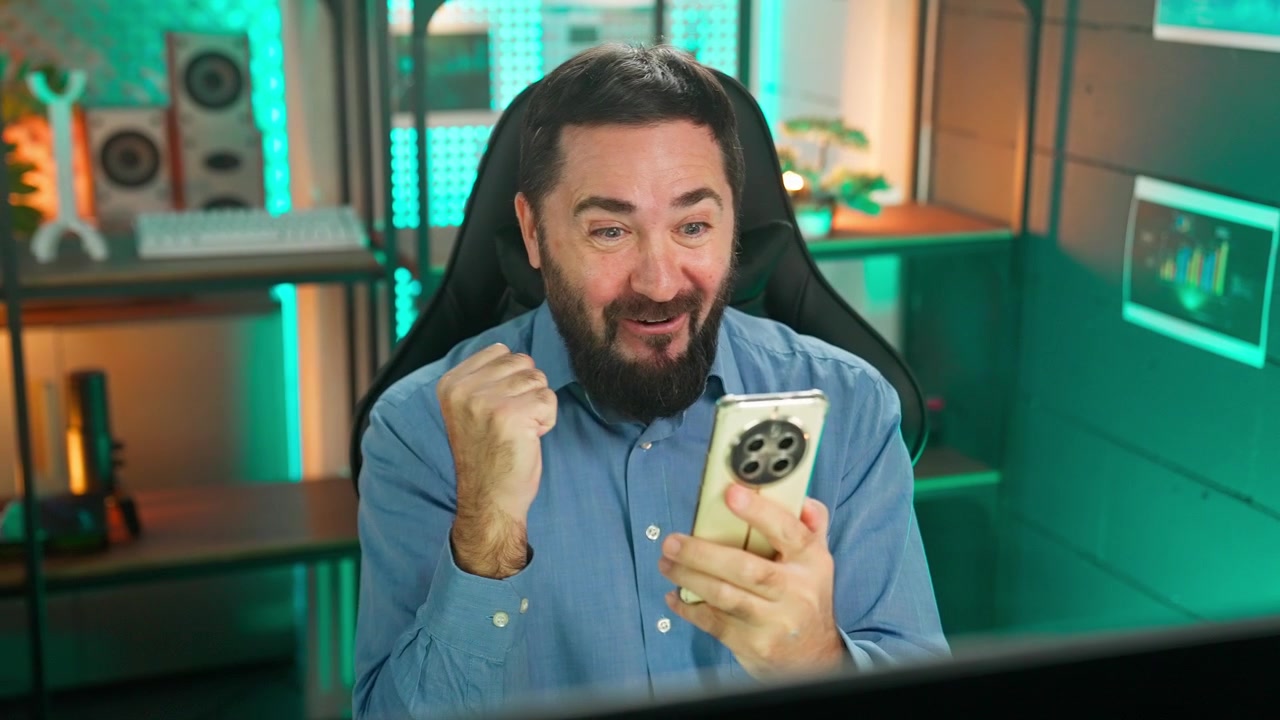 Hombre barbudo emocionado reaccionando a buenas noticias en su smartphone en una oficina moderna