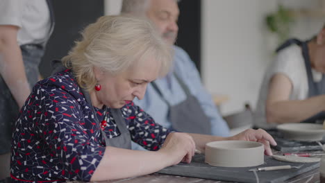 three elderly people work on a potter's wheel in slow motion