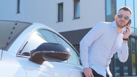 Portrait of an Attractive American Man Standing Near an Expensive Car and Talking on the Phone. Portrait of an attractive American man standing near an expensive car and talking on the phone. CFO of a sunscreen company against the of a building