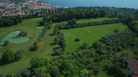 Vuelo-Aéreo-Sobre-El-Campo-De-Golf-Ca&#39;-Degli-Ulivi&#39;-Con-Vistas-A-La-Orilla-Del-Lago-De-Garda-En-El-Fondo