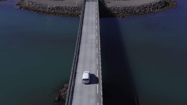 White car crossing bridge over calm river mouth at Iceland coastal land, aerial