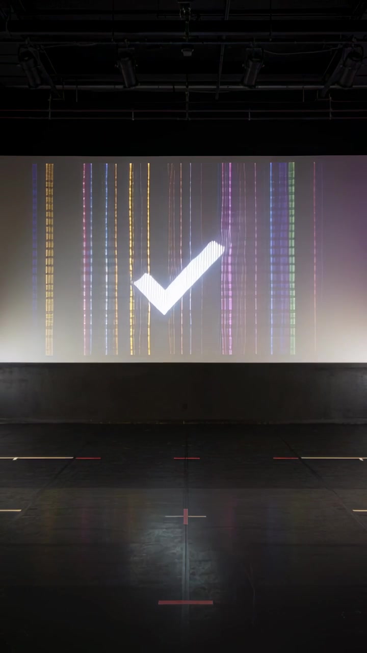 Video verticale: proiezione di un segno di spunta che si sposta al centro su un palco buio per l'allestimento, mostrando barre colorate