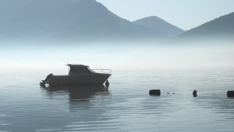 still boat and moorings in thick fog with silhouette mountain background