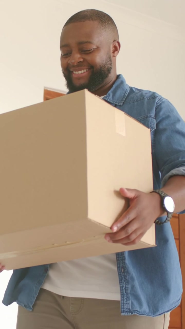 Vertical video: Entering man in denim shirt bringing package inside and adjusting grip at home door