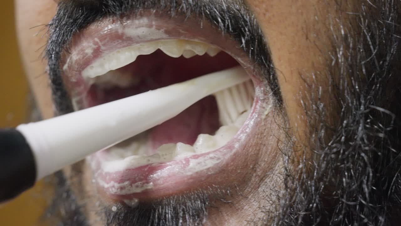 A slow-motion, close-up footage of a South Asian man brushing his teeth, with a blurred background. Dental care and hygiene concept