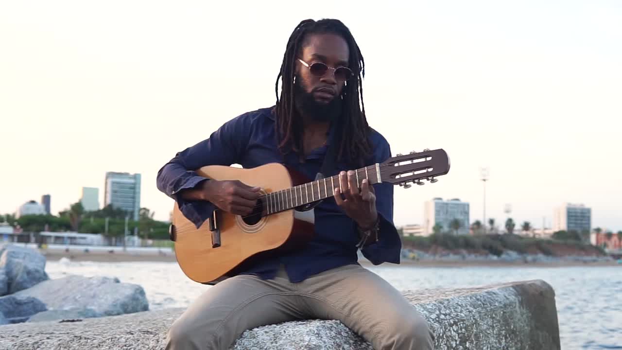 Afroamerikansk musiker spiller guitar ved kysten nær en by