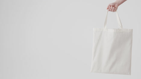 Hand-of-caucasian-woman-holding-white-bag-on-white-background,-copy-space,-slow-motion
