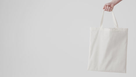 hand of caucasian woman holding white bag on white background, copy space, slow motion