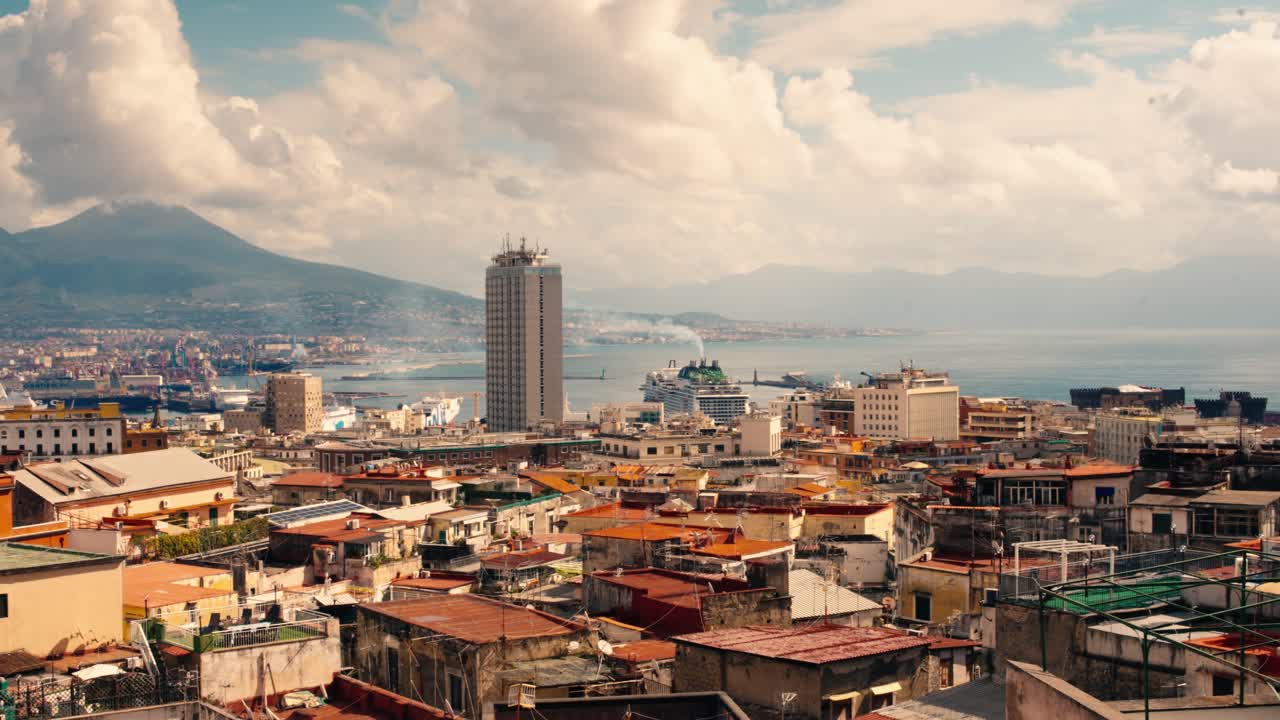 Yoğun mimarisi, liman yakınındaki modern gökdelenleri ve ikonik Vezüv Dağı fonuyla geniş Napoli şehir manzarası, bulutlu bir gökyüzü altında
