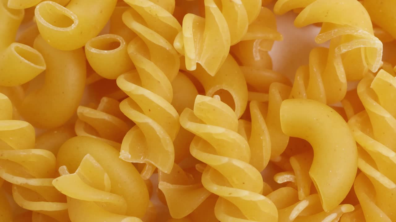 Pasta varieties cascade in slow motion against a white background, highlighting texture and form with soft lighting