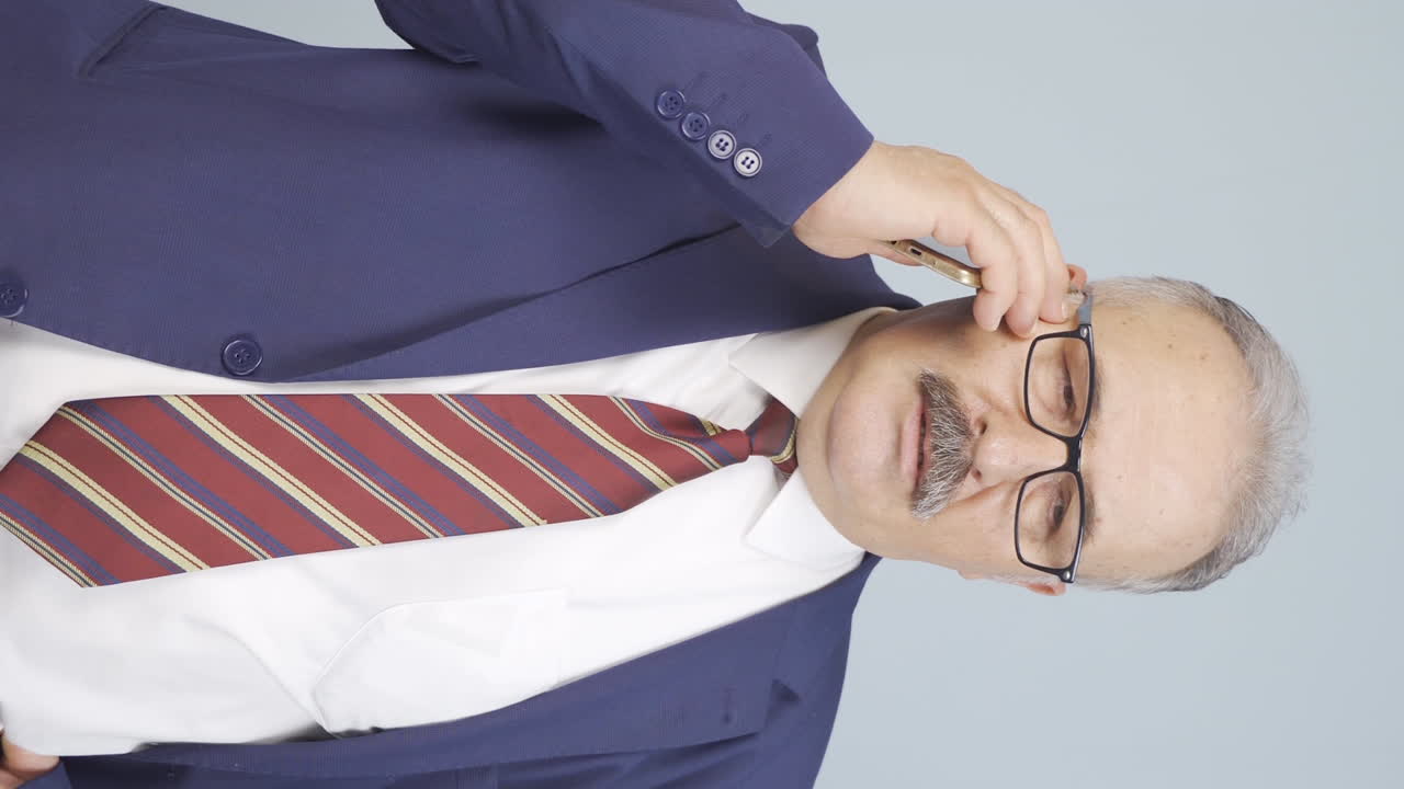 video vertical de un viejo hombre de negocios siendo interrumpido y enojado mientras habla por teléfono.