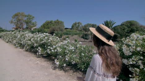 a woman in a straw hat smiling and pointing in a garden