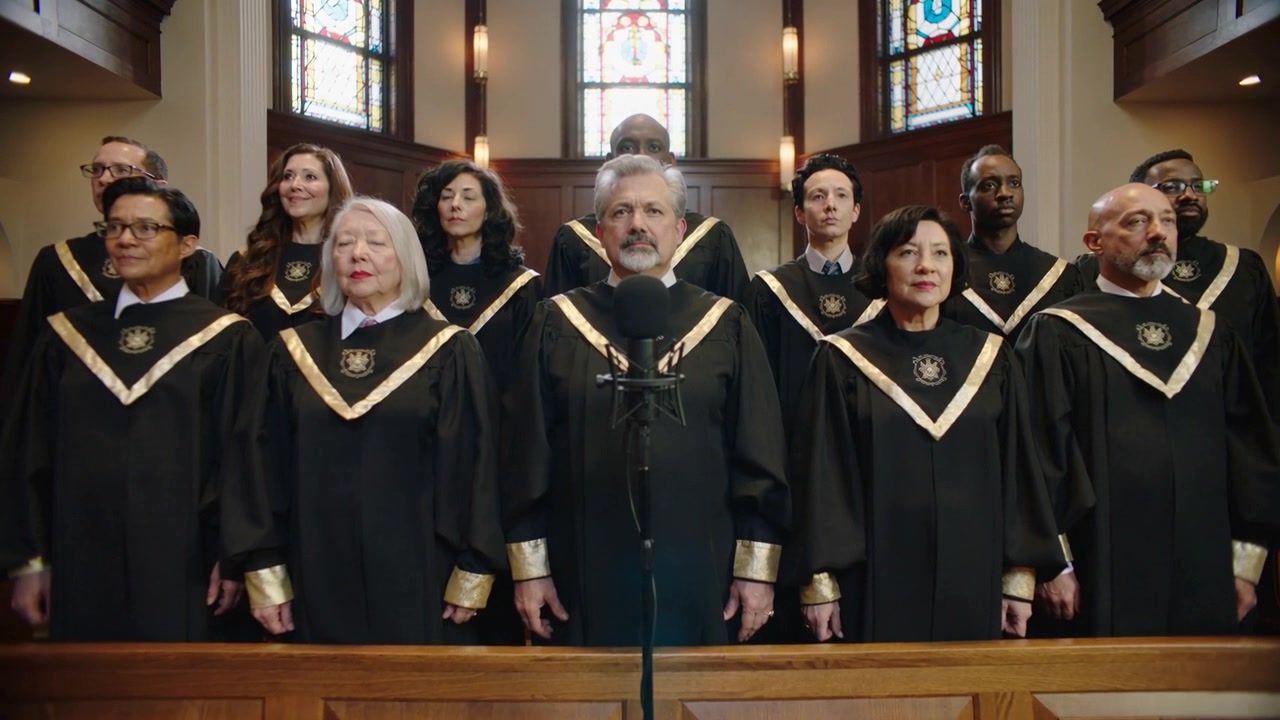 Coro che canta seguendo l'indicazione dell'inno per il culto in chiesa, indossando vesti con finiture dorate e con microfono.