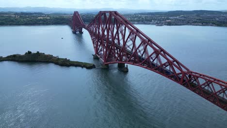 Stunning 4K drone shot of the iconic red steel Forth Bridge in Scotland, with a train passing overhead, highlighting its engineering marvel and breathtaking aerial views of the river and coastline.