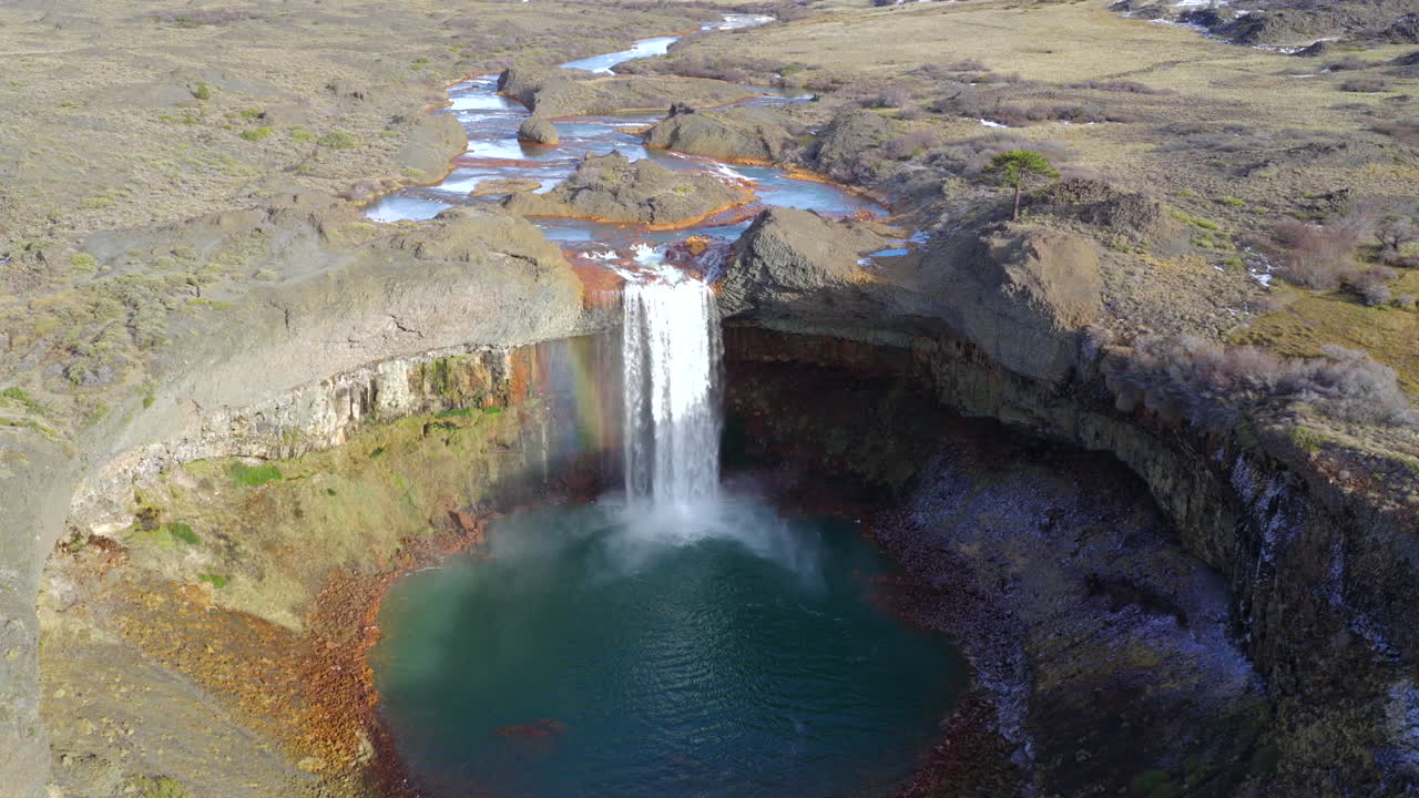 Drone descent reveals Agrio Waterfall near Caviahue, Neuquén, Argentina, as the Agrio River drops over columnar basalt into a teal plunge pool, surrounded by steppes, snow, and rugged volcanic cliffs