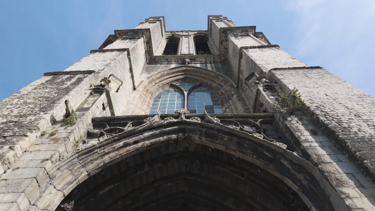 Low angle view of the impressive Saint Michael's Church bell tower in Ghent, Belgium, showcasing its intricate gothic architecture against a clear blue sky