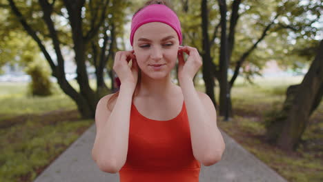 portrait of athletic sport runner girl training, listening favorite music song in earphones in park