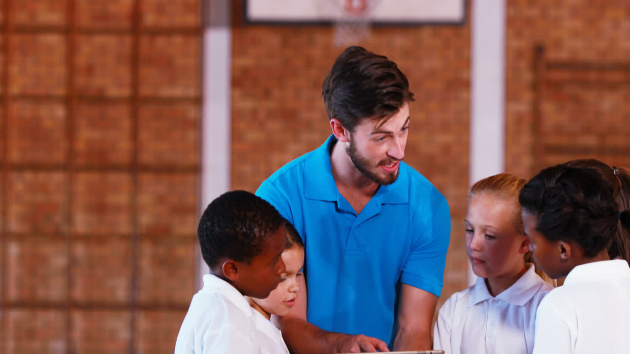 Sports teacher teaching kids on digital tablet in basketball court