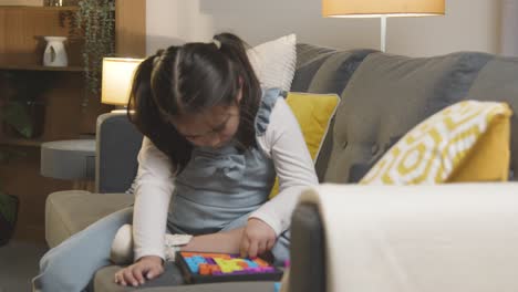 young girl on asd spectrum at home sitting on sofa solving shape puzzle 2