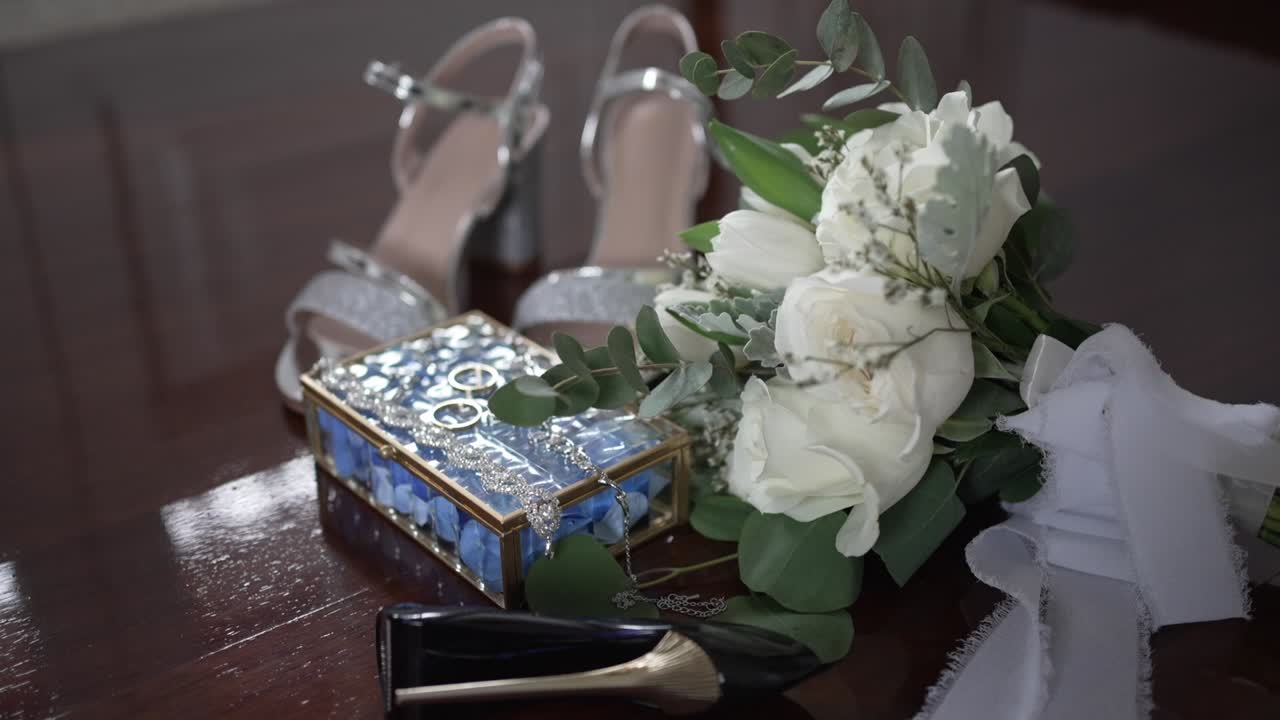 Bridal shoes, bouquet, and jewelry box with wedding rings displayed on wooden floor