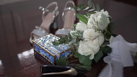 bridal shoes, bouquet, and jewelry box with wedding rings displayed on wooden floor