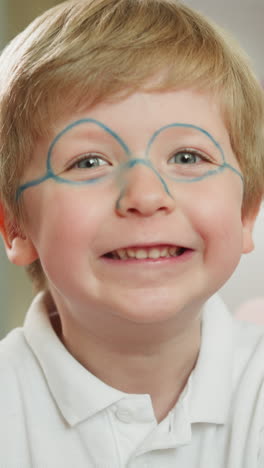 un niño pequeño con gafas pintadas sonríe mirando la cámara de cerca. el niño se ríe y muestra la lengua jugando alegremente sentado en una premisa ligera sobre un fondo borroso