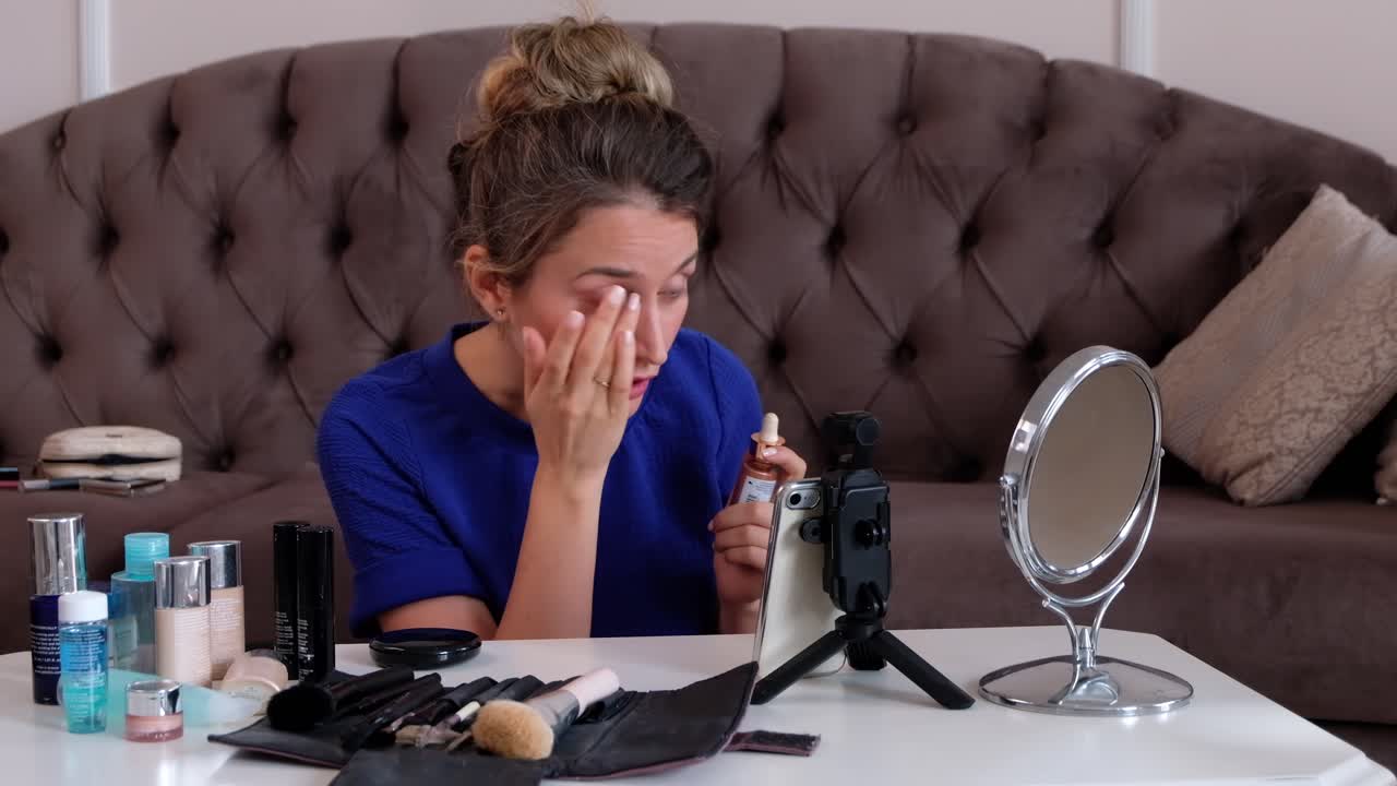 Woman in a blue T-shirt filming herself while doing her skincare at home