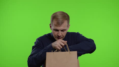 joyful man taking out sale word inscription from shopping bags, smiling satisfied with low prices