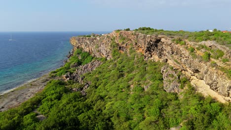 Drone-rises-above-rocky-Caribbean-cliff-to-reveal-Caracasbaai-and-Jan-Thiel-in-Vista-Royal,-Curacao