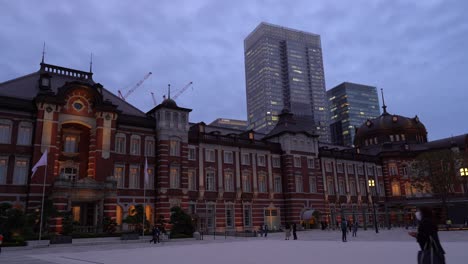 famous tokyo station at night with commuters moving around and skyscrapers in background - wide side view