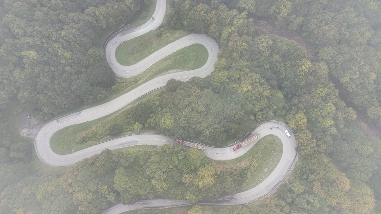 Top down aerial drone view of winding mountain road with hairpin turns through forest and fog in the Pyrenees near the border of France and Andorra