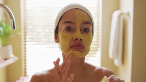 portrait of biracial woman looking into mirror and applying face mask