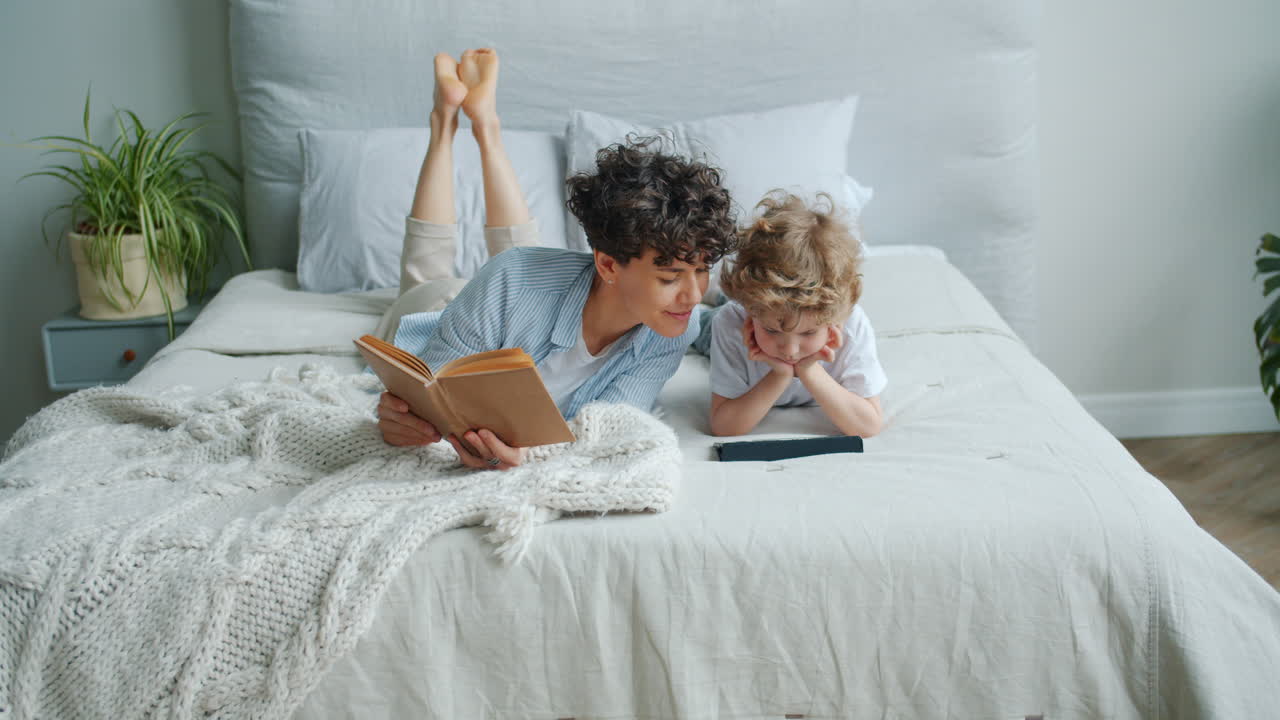 Mother and Son Relaxing in Bed, Reading and Using Tablet