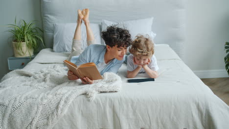 mother and son relaxing in bed, reading and using tablet