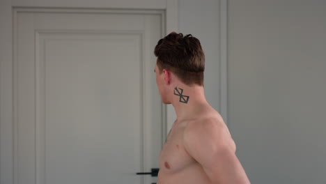 white boy standing before mirror and door pulls off neon yellow jacket to reveal neck tattoo and chest markings while posing in dynamic expressive movement inside bright modern studio setting